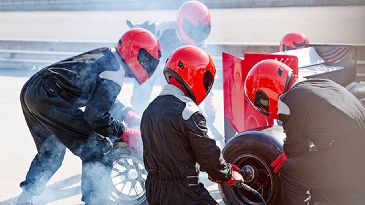 Engineers wearing red helmets changing a racing car tyre in a pit stop